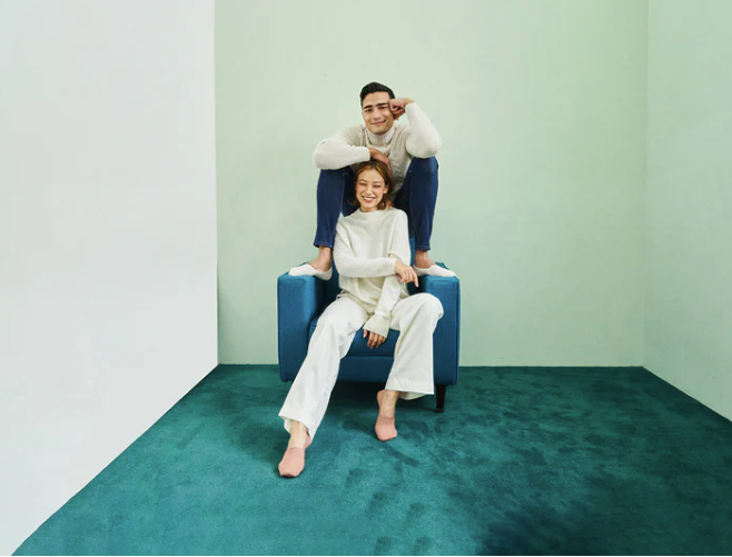 Man and women sitting in a chair in an empty carpeted room, each wearing ONDO's No Show Socks