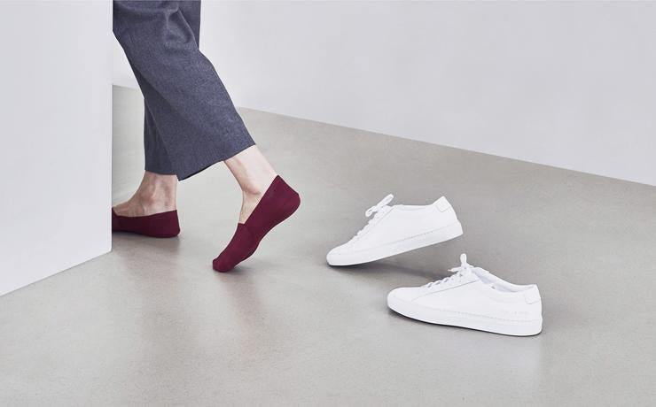 Woman stepping out of white shoes, wearing ONDO's Organic Cotton No Show Socks in Cabernet Red